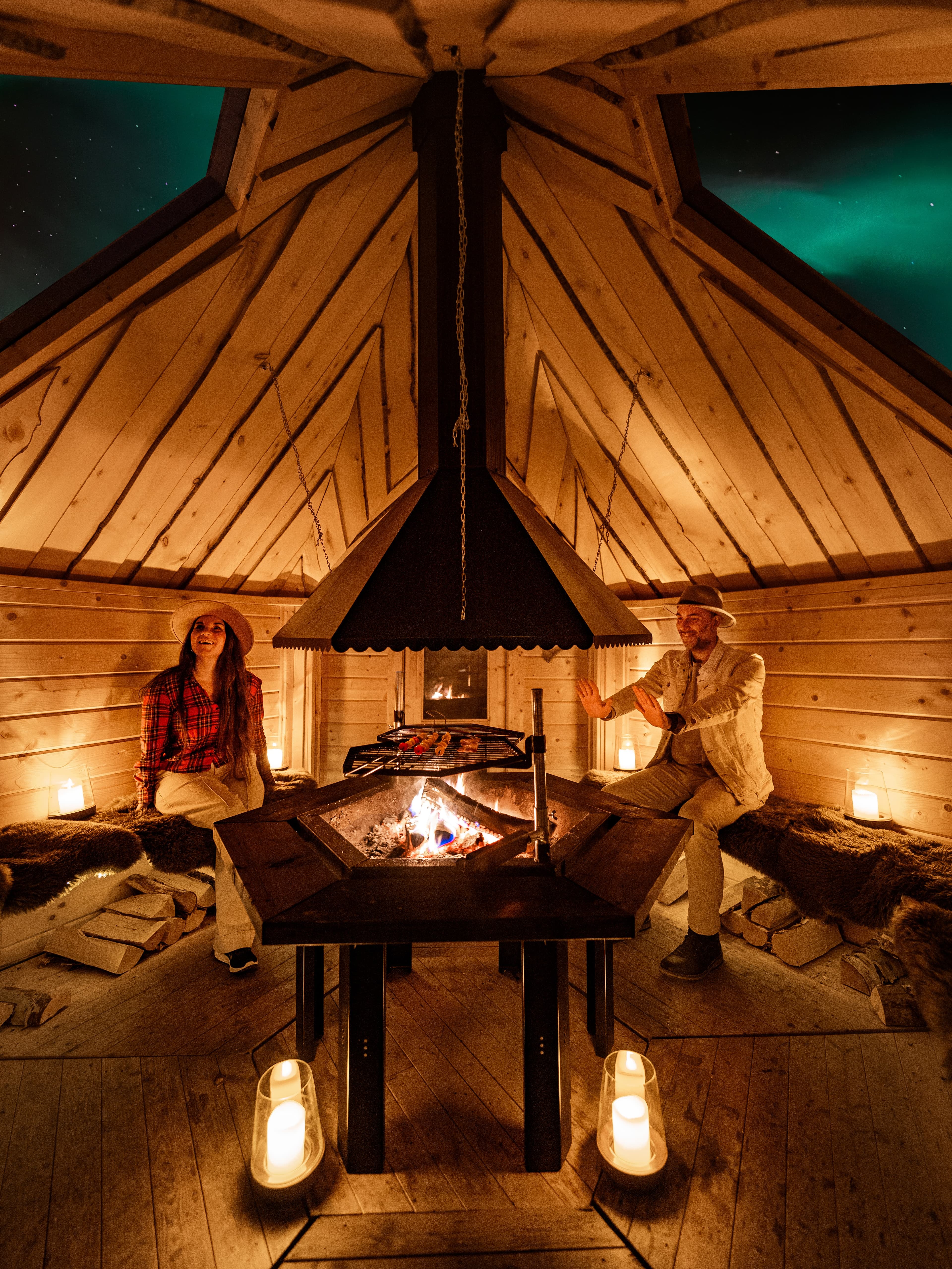 Guests warming up by the open fire inside the Aurora Hut, Northern Lights through the roof window
